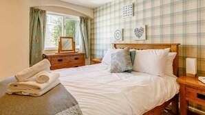 Un dormitorio con cama, mesita de noche, cómoda, ventana con cortinas y pared con diseño escocés.