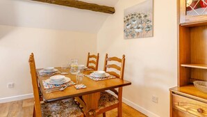 Un comedor con una mesa de madera dispuesta para cuatro, sillas, un cuadro en la pared y un armario de madera.