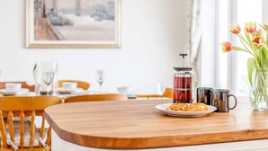 Ein Essbereich mit einem Holztisch, einer Auswahl an Gebäck, einer Kaffeemaschine und einer Tulpenvase.
