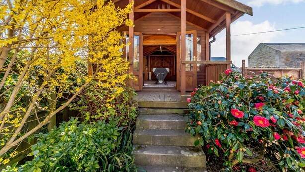 Eine Holzjagdhaus mit Veranda, ein Grill davor und ein Steinhaus im Hintergrund.