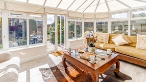 Ein Wintergarten mit einer Couch, einem Couchtisch und Blick auf den Garten.