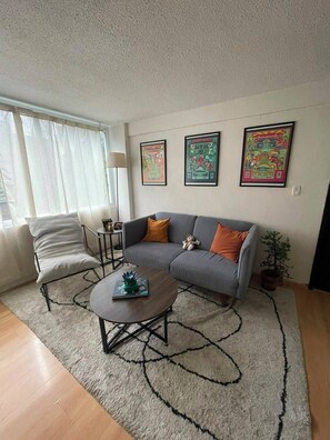 Ein Wohnzimmer mit grauem Sofa, einem weißen Sessel, einem Couchtisch und einem Teppich mit abstraktem, schwarzem Muster.