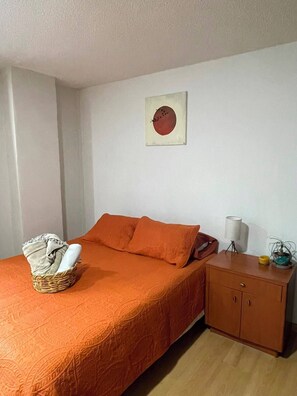 Ein Zimmer mit einem Bett, einem Nachttisch, einer Lampe und einem an der Wand hängenden Kunstwerk.