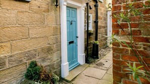 A stone building with a blue door, a small garden, and a brick wall. - 2 Bed in Whitby (oc-87059) (Robin Hood's Bay)