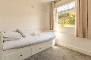 A single bed with storage drawers, a window with curtains, and a view of greenery outside. - 3 Bed in Perranporth (oc-87126) (Perranporth)