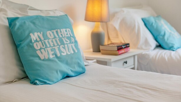 A bed with a pillow that reads 'MY OTHER OUTFIT IS A WETSUIT' and a bedside lamp. - 3 Bed in Perranporth (oc-87126) (Perranporth)
