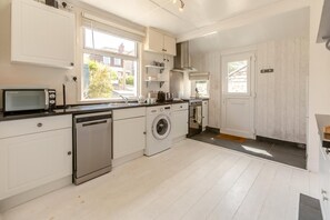 A compact kitchen with white cabinetry, a dishwasher, a washing machine, and a microwave. - 3 Bed in Perranporth (oc-87126) (Perranporth)