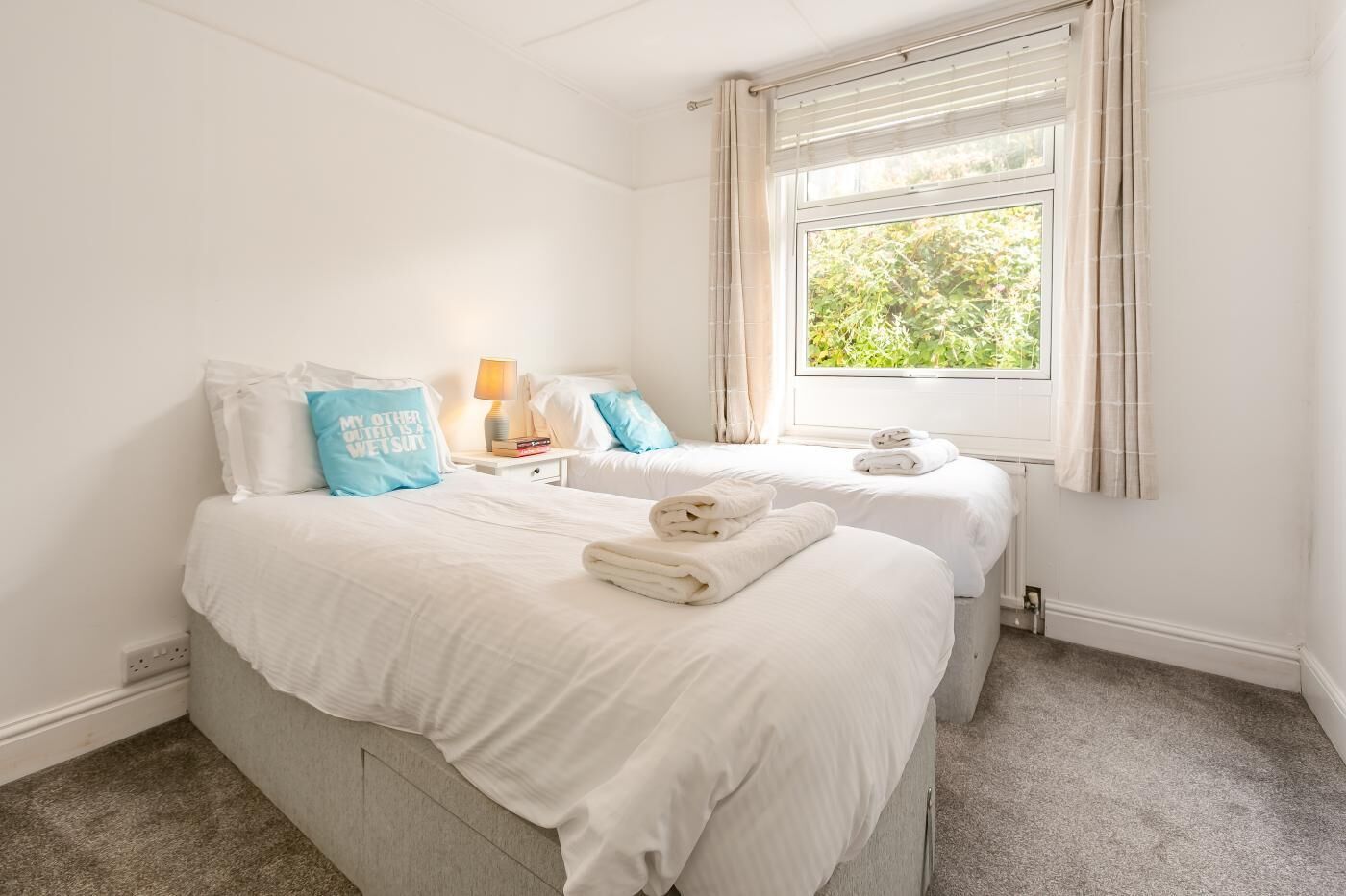 Une chambre d’hôtel avec deux lits, une fenêtre avec des rideaux, une table de chevet avec une lampe et des serviettes sur les lits.