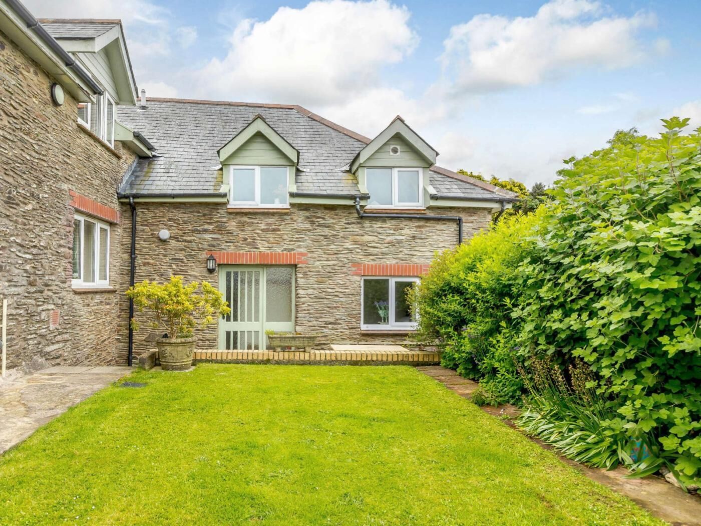 A stone house with a sloped roof, a small front porch, and a well-maintained lawn.
