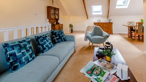 A cozy living room with a sofa, armchair, dining table, and a bookshelf. - 2 Bed in Ilfracombe (oc-86940) (Berrynarbor)