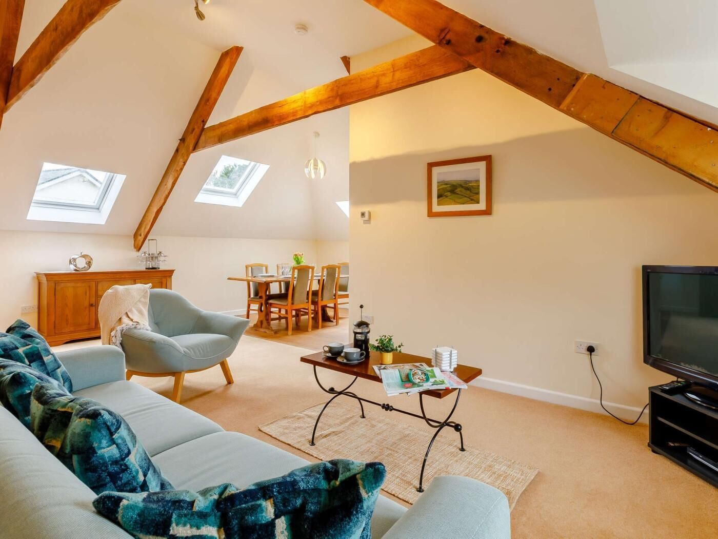 Un espacio tipo loft con techo alto, vigas de madera a la vista, sofá, mesa de comedor y televisor.