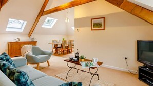 A loft-style room with a high ceiling, exposed wooden beams, a sofa, a dining table, and a television. - 2 Bed in Ilfracombe (oc-86940) (Berrynarbor)