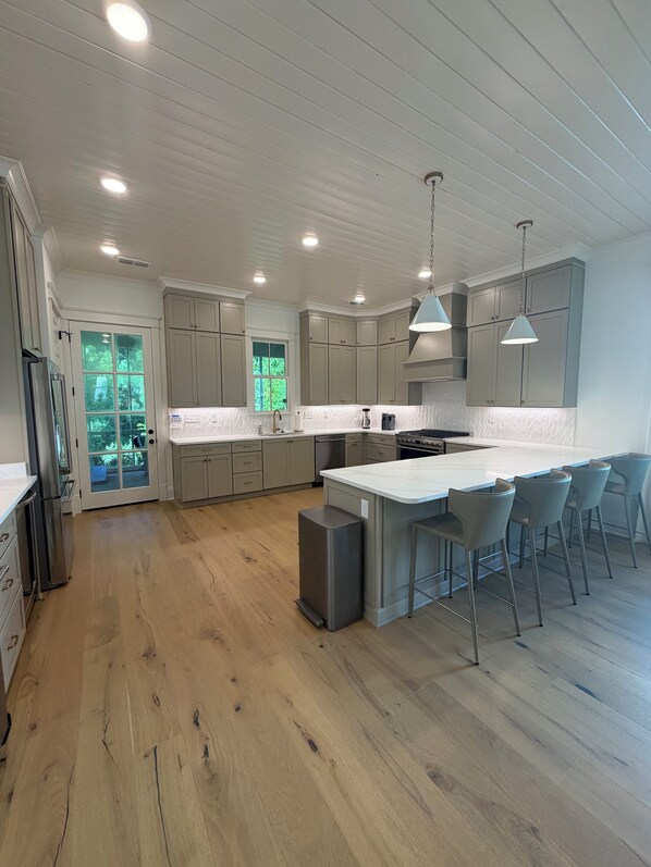 A modern kitchen with wooden flooring, built-in cabinets, a central island with bar stools, and pendant lighting. - Upscale New Build • 3BR/3.5BA • Minutes to Campus and the Square (Oxford)