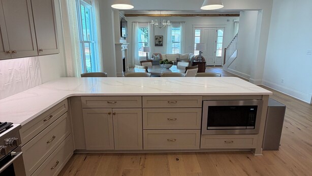 A modern kitchen with wooden flooring, white cabinetry, and pendant lighting.