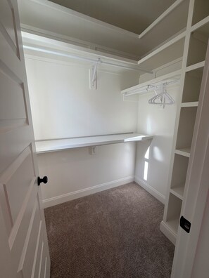 A walk-in closet with white shelving, a hanging rod, and a carpeted floor.