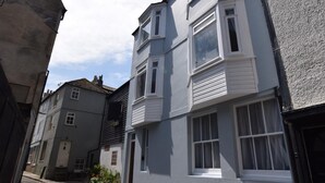 Eine enge Straße mit zweistöckigen Gebäuden, eines davon mit einem Balkon und das andere mit einer sichtbaren Haustür.