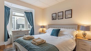 Ein Schlafzimmer mit Bett, Nachttischen, einem Fenster mit Vorhängen und Wandbildern.