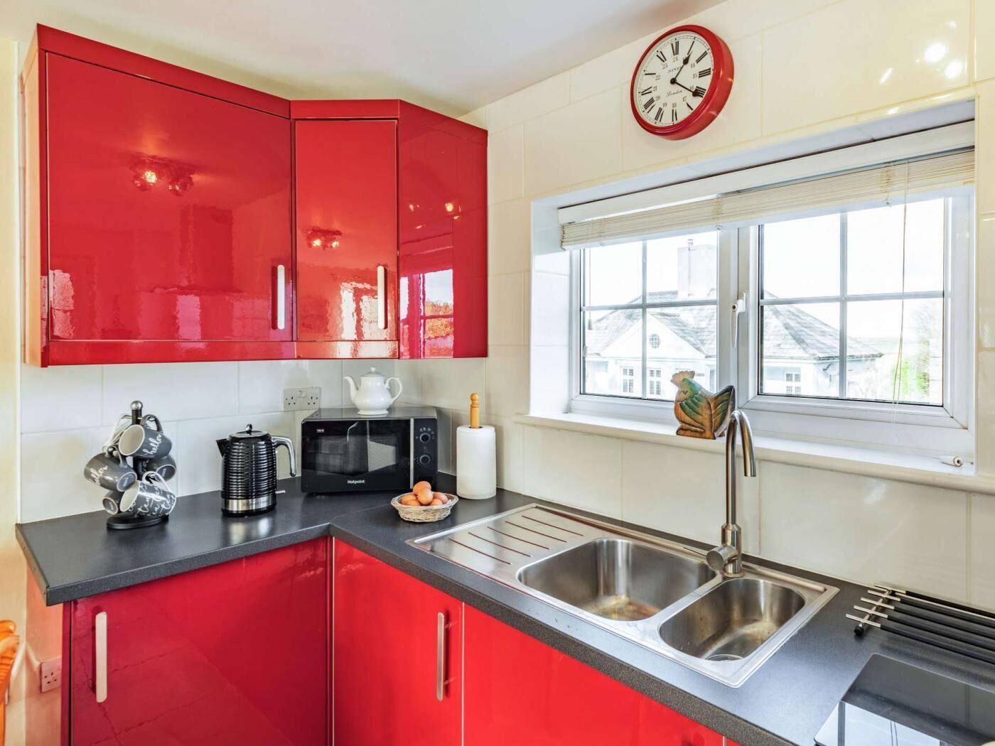 A kitchen with red cabinets, a microwave, a sink, and a window with a view.