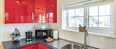A kitchen with red cabinets, a microwave, a sink, and a window with a view.