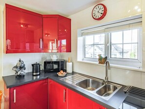 A kitchen with red cabinets, a microwave, a sink, and a window with a view. - 2 Bed in Bude (oc-86920) (Kilkhampton)