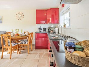 A modern kitchen with red cabinets, a dining table with chairs, and a variety of kitchen appliances. - 2 Bed in Bude (oc-86920) (Kilkhampton)
