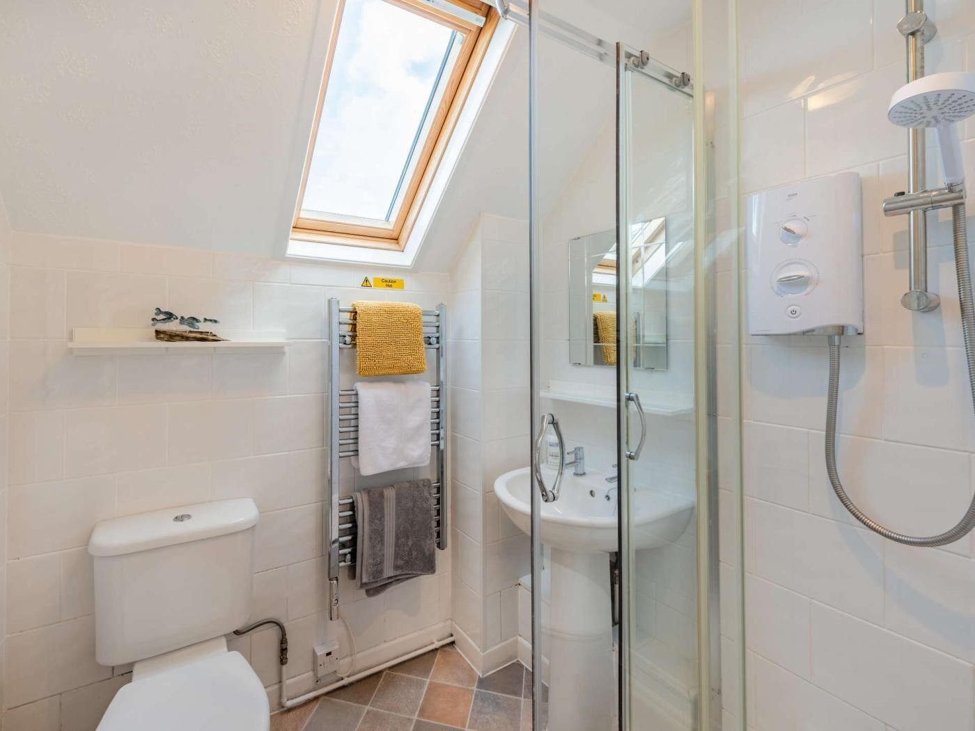 A modern bathroom with a skylight, glass shower enclosure, white tiles, and a toilet.