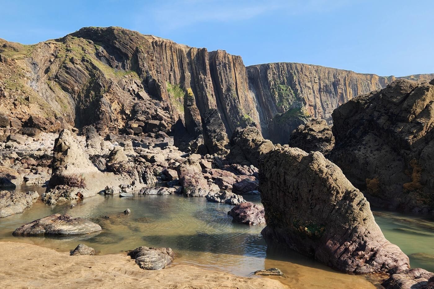A rocky coastal landscape with clear water, large boulders, and steep cliffs.