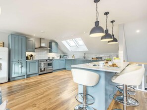 A modern kitchen with light blue cabinets, a central island with bar stools, a built-in oven, and a skylight. - 3 Bed in Aberdovey (oc-86932) (Aberdovey)
