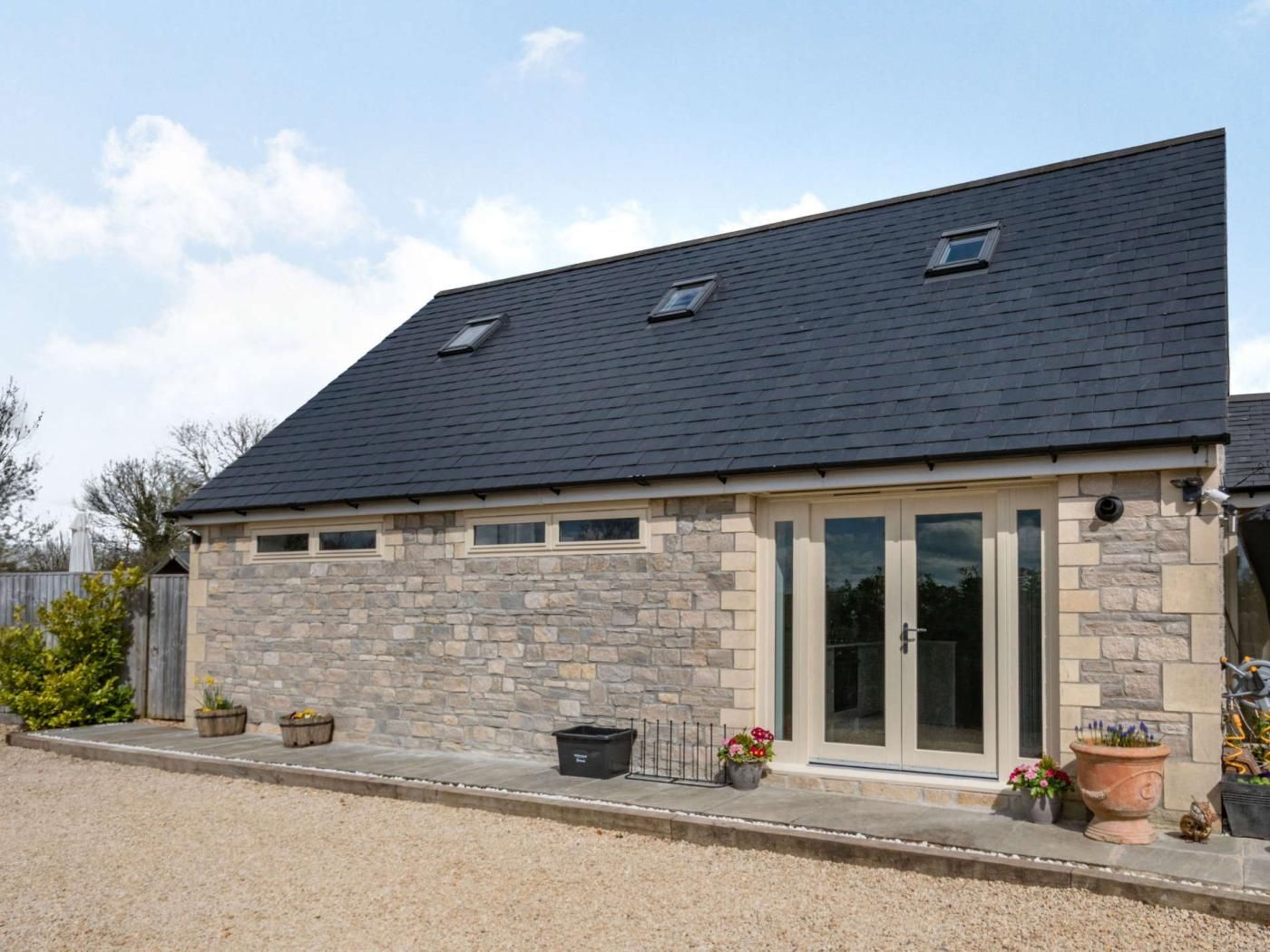 A two-story stone building with a dark roof, large glass doors, and a gravel driveway.