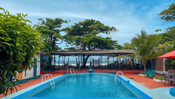 Une piscine avec vue sur l’océan, entourée d’arbres et dotée d’un espace salon abrité.