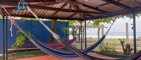 Una hamaca debajo de un techo de metal, una pared azul y vista al océano.