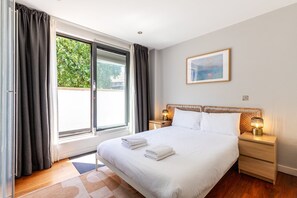 A hotel room with a large bed, two bedside tables with lamps, a window with curtains, and a painting on the wall. - Bright Lambeth Apartment by Waterloo (London)