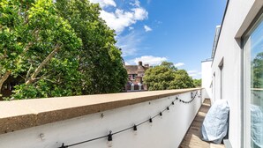 A balcony with a string of lights, a white wall, and a view of a building with a red roof. - Bright Lambeth Apartment by Waterloo (London)
