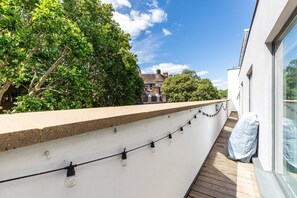 Ein Balkon mit Lichterkette, einer weißen Wand und Blick auf ein Gebäude mit rotem Dach.