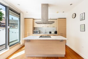 A modern kitchen with a large island, built-in appliances, and a view through a sliding door. - Bright Lambeth Apartment by Waterloo (London)