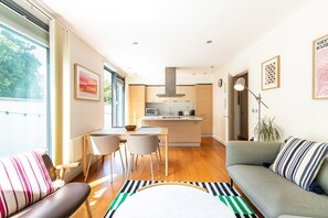 Ein modernes Wohnzimmer mit einer Couch, einem Essbereich mit Stühlen, einer Küche mit Kochinsel und einem großen Fenster, das für natürliches Licht sorgt.
