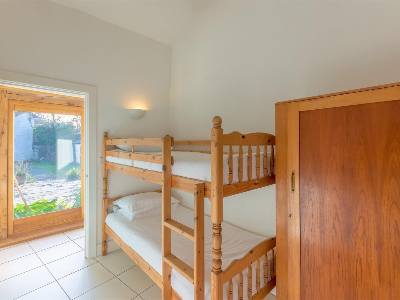 Un letto a castello con una testiera in legno, un armadio e una porta che dà sul giardino.