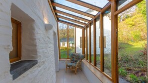 Een zonnige kamer met een glazen dak, een rieten stoel en uitzicht op een tuin.