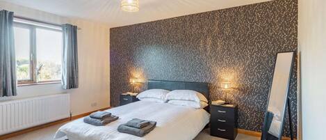 Une chambre à coucher avec un lit, des lampes de chevet, un miroir et une fenêtre avec des rideaux.