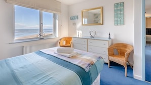 Quarto com cama, cômoda, cadeira, espelho e vista para o mar.
