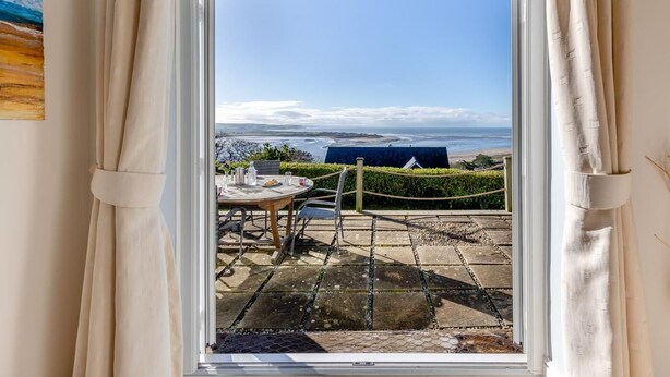 Um quarto com vista para o oceano, uma mesa de jantar com cadeiras e uma janela com cortinas.