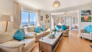 Sala de estar com sofá, mesa de centro e vista para o mar.