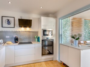 Eine moderne Küche mit weißen Schränken, einem eingebauten Backofen, einer Mikrowelle und einem großen Fenster mit Blick auf einen Strand.