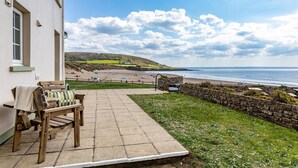 Eine Terrasse mit einer hölzernen Bank und einer Steinmauer, mit Blick auf einen Strand und das Meer.