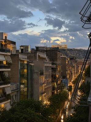 A cityscape with modern buildings, a prominent ancient structure in the background, and a river reflecting city lights. - Athens Acropolis Balcony  (Athina)