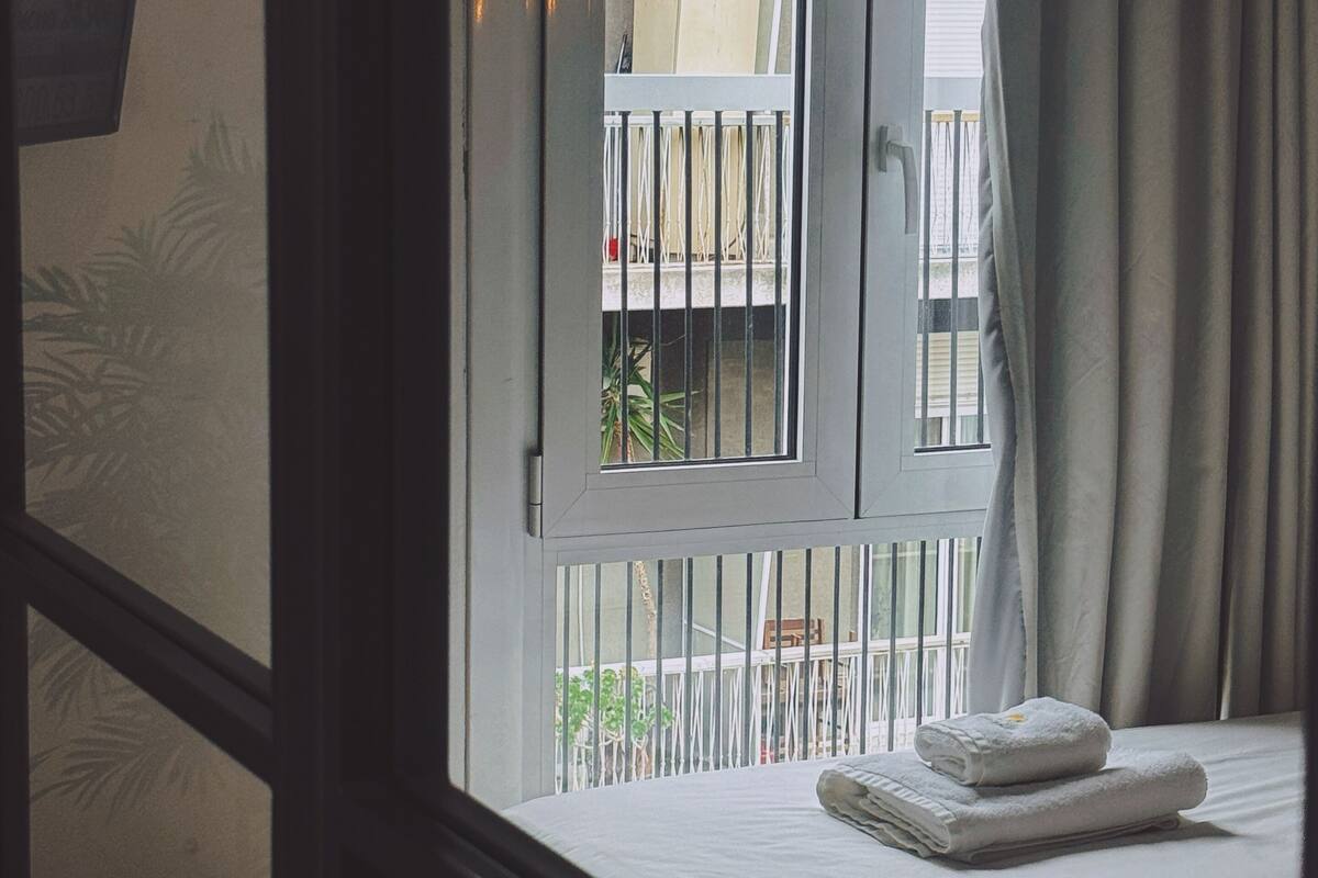 Une chambre à coucher avec un lit, une fenêtre avec des rideaux et une vue sur un balcon doté d’une balustrade.