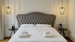 A modern bedroom with a tufted headboard, a large bed with white linens, two bedside tables with lamps, and a bench at the foot of the bed.