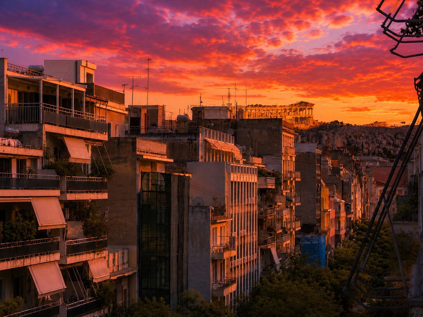 Un edifici de diverses plantes amb balcons, un terrat pla i un turó al fons.