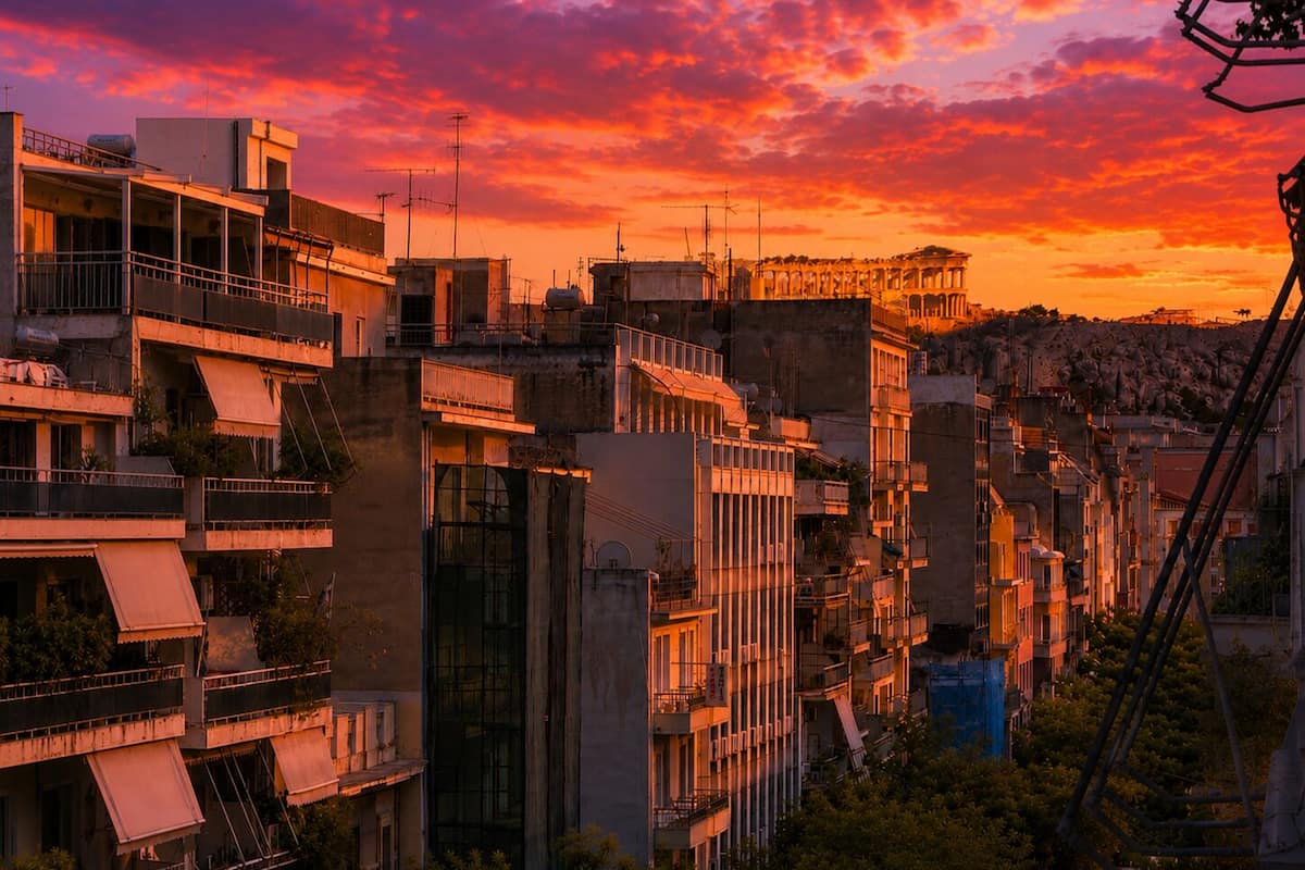 Um edifício de vários andares com varandas, um telhado plano e uma encosta ao fundo.