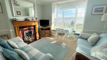 A living room with a fireplace, a television, a dining area with a table and chairs, and a large window with a view.